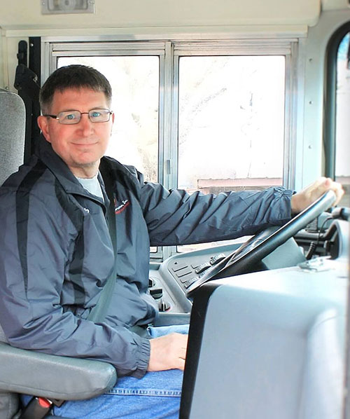 Young man sitting in the driver's seat of a school bus with a checklist