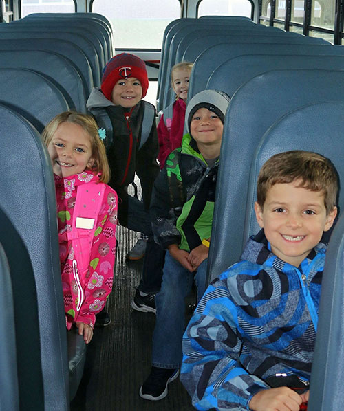 Kids sitting in a school bus waving to the camera