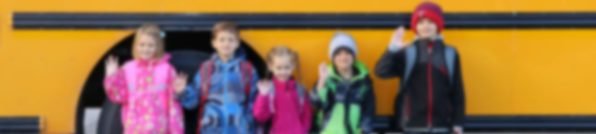 Elementary students lined up in front of a yellow school bus waving